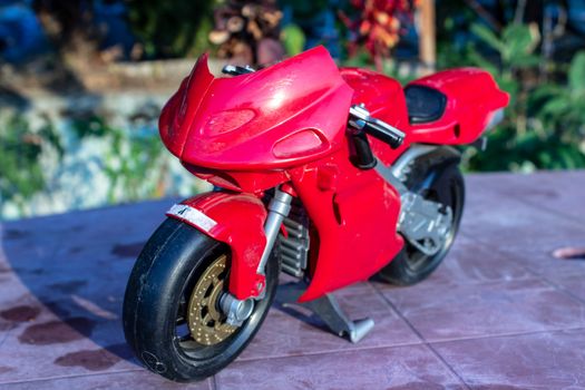 a isolated closeup red toy motorcycle with cold colors. photo has taken from a garden.