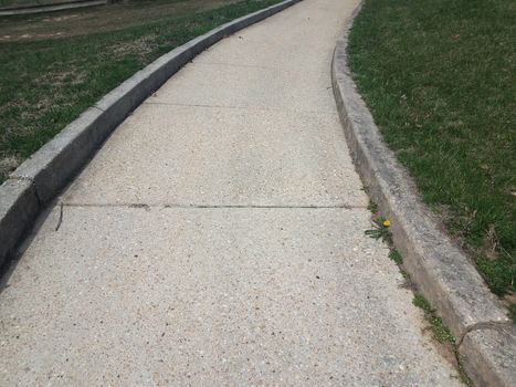 grey cement sidewalk or path with curb and green grass or lawn