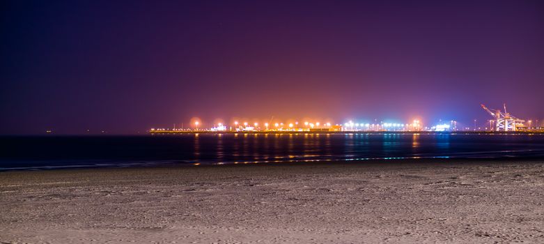 the coastline of Blankenberge beach lighted by night, colorful lights on the industry terrain in the distance