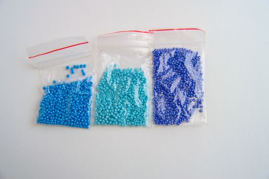 Set of three plastic bags with blue glass beads with gradient color on white background, beaded embroidery accessories.