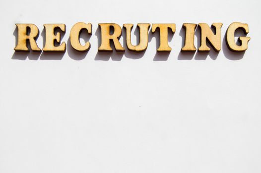 The word recruiting is written in wooden letters on a white background, the concept of hiring employees, recruitment in business and army.