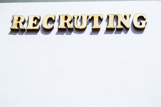 The word recruiting is written in wooden letters on a white background, the concept of hiring employees, recruitment in business and army.