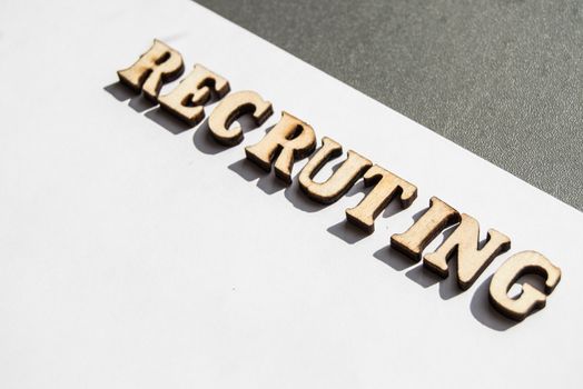 The word recruiting is written in wooden letters on a white background, the concept of hiring employees, recruitment in business and army.