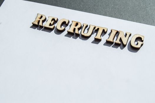 The word recruiting is written in wooden letters on a white background, the concept of hiring employees, recruitment in business and army.