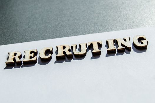 The word recruiting is written in wooden letters on a white background, the concept of hiring employees, recruitment in business and army.