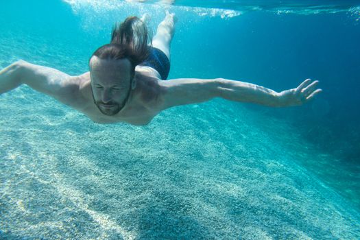 Bearded man diving on a breath hold swimming under water view