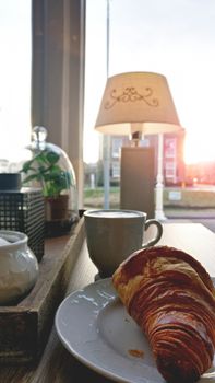 Cup of coffee and fresh baked croissants on plate for breakfast on the table near the window with city view