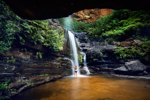 Cooling off in a mountain oasis and waterfall. A woman escapes the summer heat visiting a mountain oasis with fresh waterfalls, letting the cooling water flow onto her body