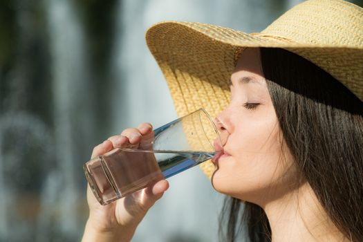 The beautiful girl in a hat drinks water in a glass