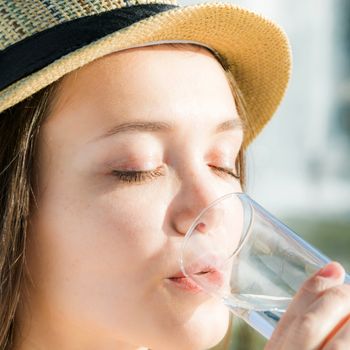 The beautiful girl in a hat drinks water in a glass