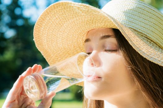 The beautiful girl in a hat drinks water in a glass