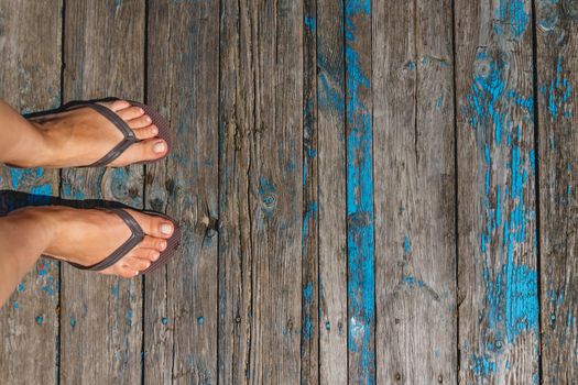 Top view, photo of female legs in beach flip flops on a wooden old floor. Photos on vacation, beach, summer.