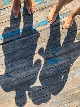 Top view, photo of bare feet and a pair of shadows on a wooden old floor. Photos on vacation, beach, summer.