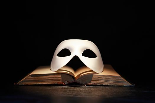 Classical white Venetian mask on old book against dark background