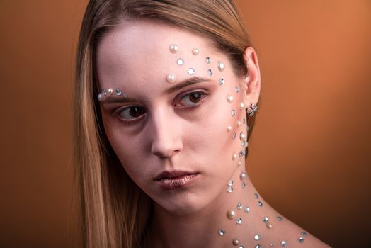 Portrait of a girl with original and creative makeup with white and pearl rhinestones