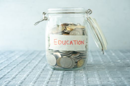 Coins in glass money jar with education label, financial concept. 