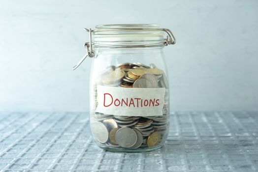 Coins in glass money jar with donations label, financial concept.