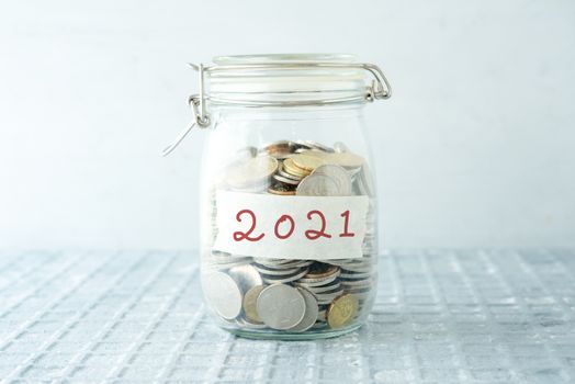Coins in glass money jar with 2021 label, financial concept.