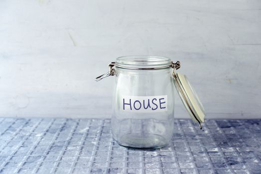 Empty glass money jar with house label, financial concept.