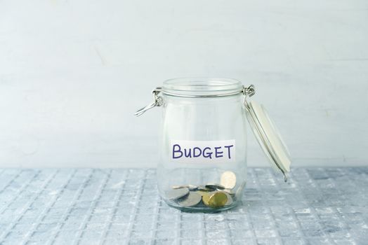 Little coins in glass money jar with budget label, financial concept.