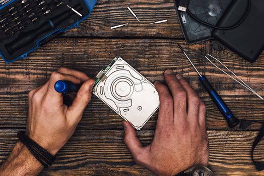 Two Male Hands with Screwdriver Disassemble HDD on Wooden Background