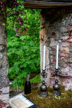 Candles in a candlestick, bottle of champagne and two glasses in moss at stone ruins. Wedding celebration simbols in outdoors. 