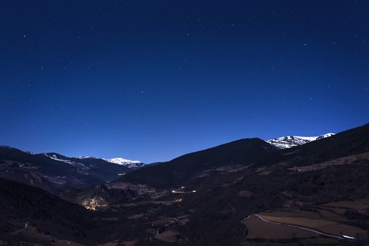 night mountain landscape under the starry sky, you can see the lights of the houses in the valley and some snowy mountains