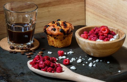 Cottage cheese with raspberries, coffee in a cup and blueberry muffin for breakfast with scattered berries, grains of curd and coffee beans