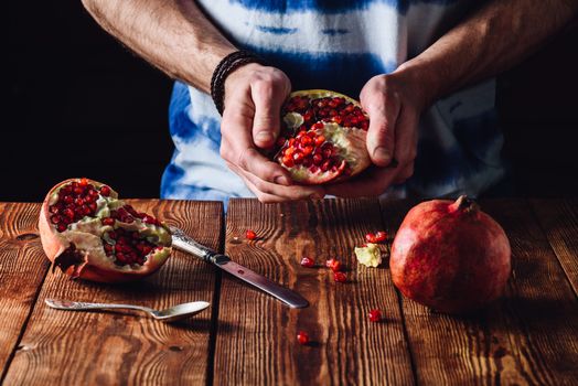 Opened Pomegranate in the Hands. Other Half and Some Seeds on Table.