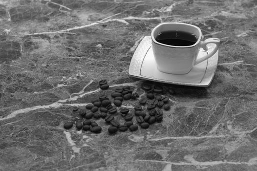 A cup of black coffee and grains lie on a marble table.