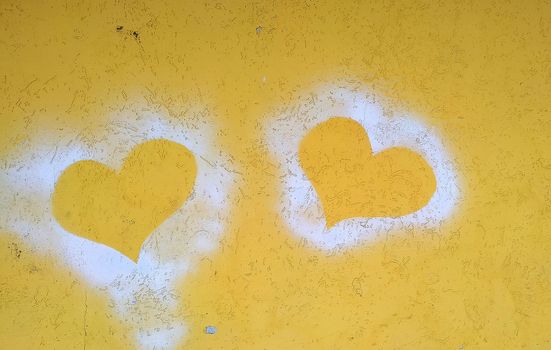 Silhouettes of two hearts on a yellow concrete wall. Close-up.