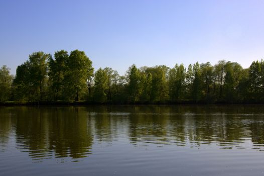 The view of the forest lake, the shores are reflected in the calm surface of the water. The picture was taken on a warm spring day, with natural light.