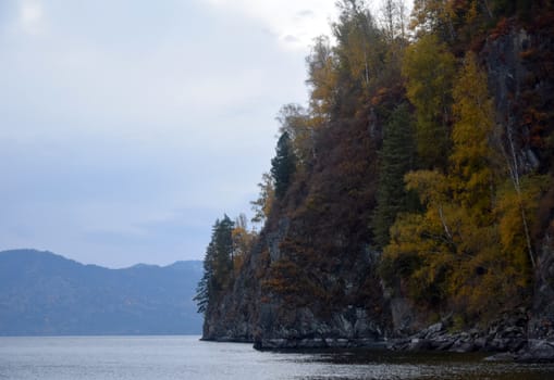 East rocky shore of Lake Teletskoye, cliffs covered with a beautiful forest. The picture was taken on an autumn day, with natural light.