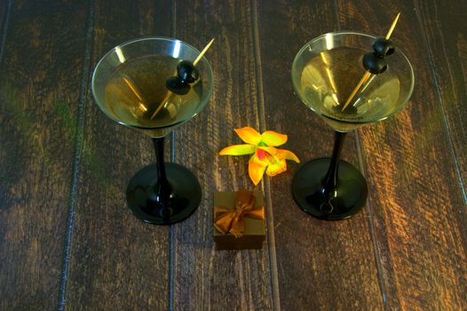 Martini glass with olives with gift box and yellow orchid on a wooden table Close-up.