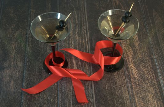 Two martini glasses with olives, with a scarlet ribbon on a wooden table Close-up.