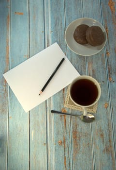 A cup of tea, two chocolate cakes and a sheet of paper with a pencil on a wooden table. Close-up.