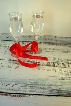 Two glasses with champagne, connected by a scarlet satin ribbon on a wooden table.Close-up.