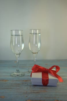 Two glasses with champagne and gift box with satin ribbon on a wooden table. Close-up.