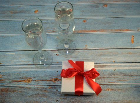 Two glasses with champagne and gift box with satin ribbon on a wooden table. Close-up.