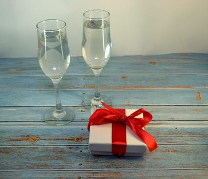 Two glasses with champagne and gift box with satin ribbon on a wooden table. Close-up.