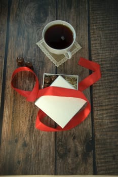 A cup of tea, a white box of chocolates with a red satin ribbon on a wooden table. Close-up.