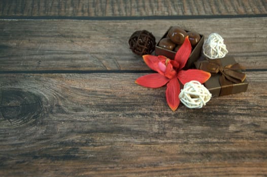 A box of chocolates, decorative balls, a bud of red orchid on a wooden table. Close-up.