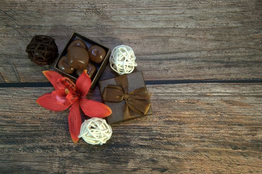 A box of chocolates, decorative balls, a bud of red orchid on a wooden table. Close-up.