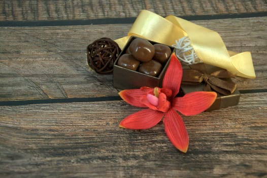 A box of chocolates, decorative balls, a bud of red orchid and beige ribbon on a wooden table. Close-up.