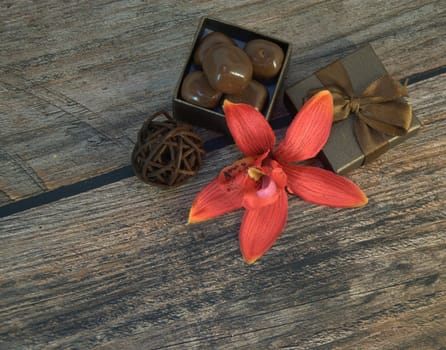 A box of chocolates, decorative balls, a bud of red orchid on a wooden table. Close-up.