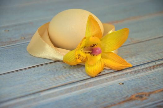 Easter egg with a yellow satin ribbon and a bud of an orchid on a wooden table. Close-up.
