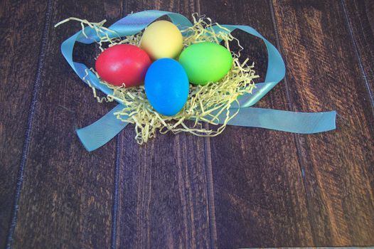 Painted Easter eggs in a nest of straw on a blue ribbon lie on a wooden table. Close-up.