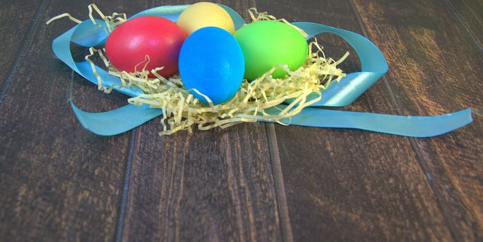 Painted Easter eggs in a nest of straw on a blue ribbon lie on a wooden table. Close-up.