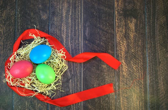 Painted Easter eggs in a nest of straw on a scarlet ribbon lie on a wooden table. Close-up.