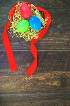 Painted Easter eggs in a nest of straw on a scarlet ribbon lie on a wooden table. Close-up.